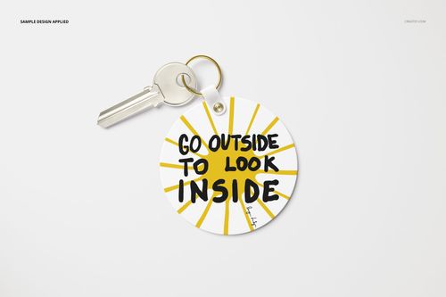 Circular key tag mockup with yellow sun rays and bold black lettering, shown from a top view with a silver key.