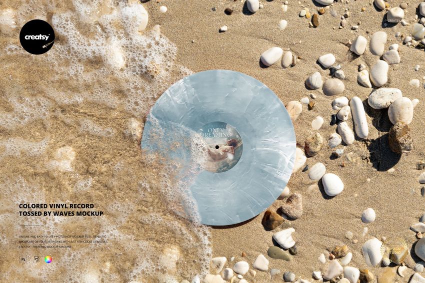 Blue colored vinyl record lying on sandy beach with foamy waves and scattered white stones, top view mockup.
