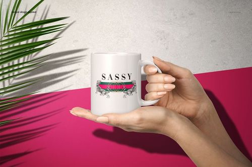 White 11oz mug with a bold pink and green stripe and 'SASSY' text, held by two hands against a pink and gray background.