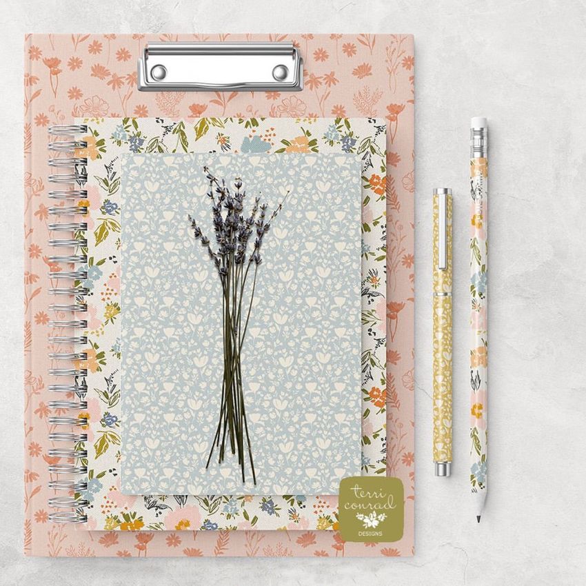 Stationery mockup featuring a clipboard, spiral notebook, and pencils with pastel floral patterns on a light surface.