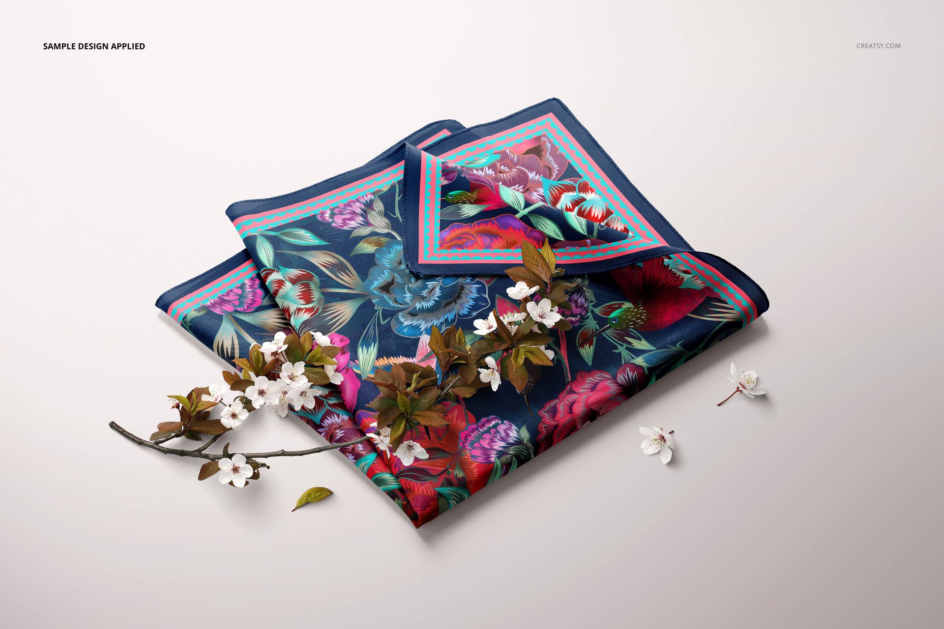 Colorful square silk scarf mockup featuring botanical designs, shown folded with decorative white flowers nearby.