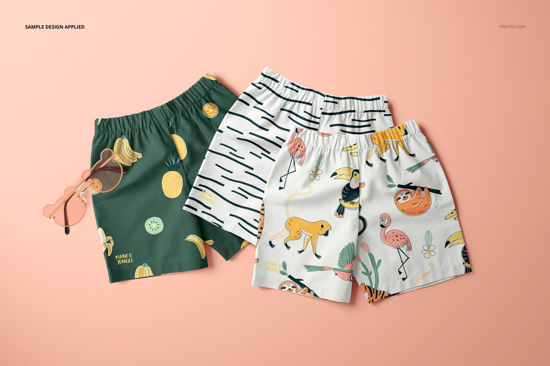 Set of three kids shorts mockup featuring colorful fruit and animal designs, arranged on a pastel pink surface.
