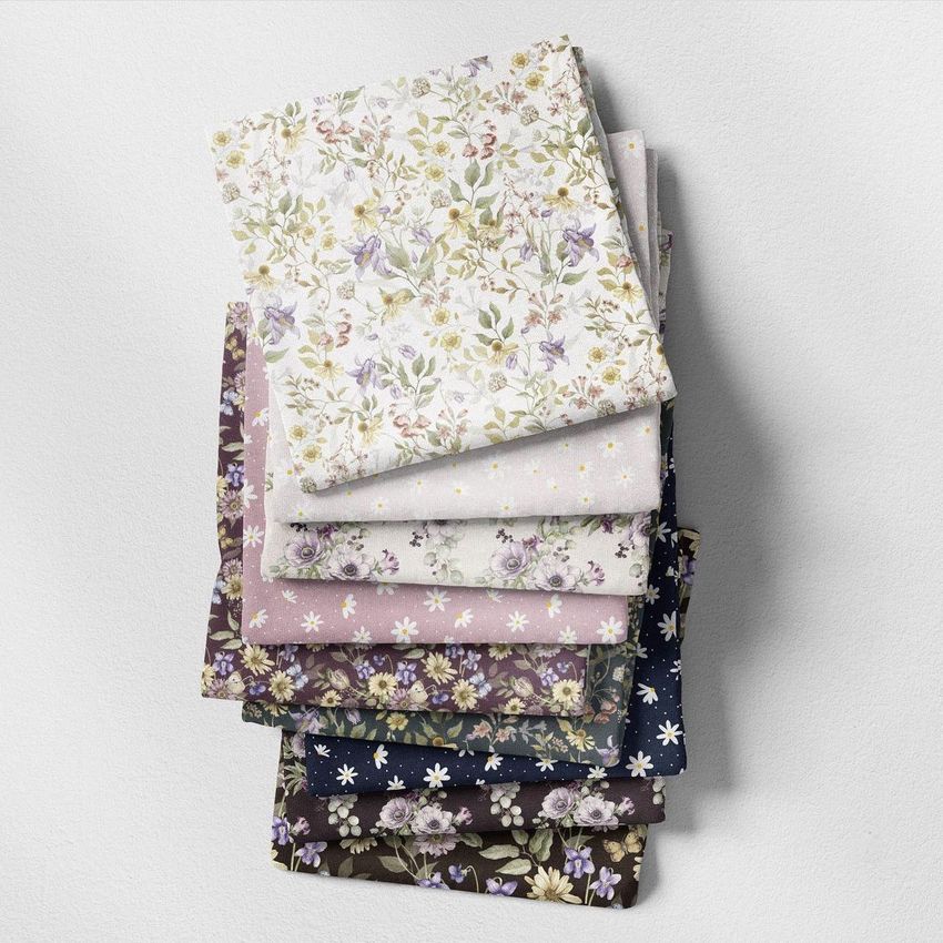 Fabric stack mockup showing several folded fabrics with floral patterns in pastel and dark colors on a light surface.