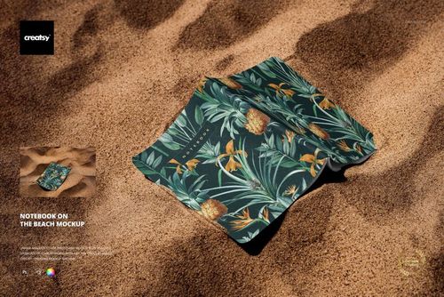 PSD mockup featuring a pair of notebooks with green and yellow botanical designs placed on textured beach sand.