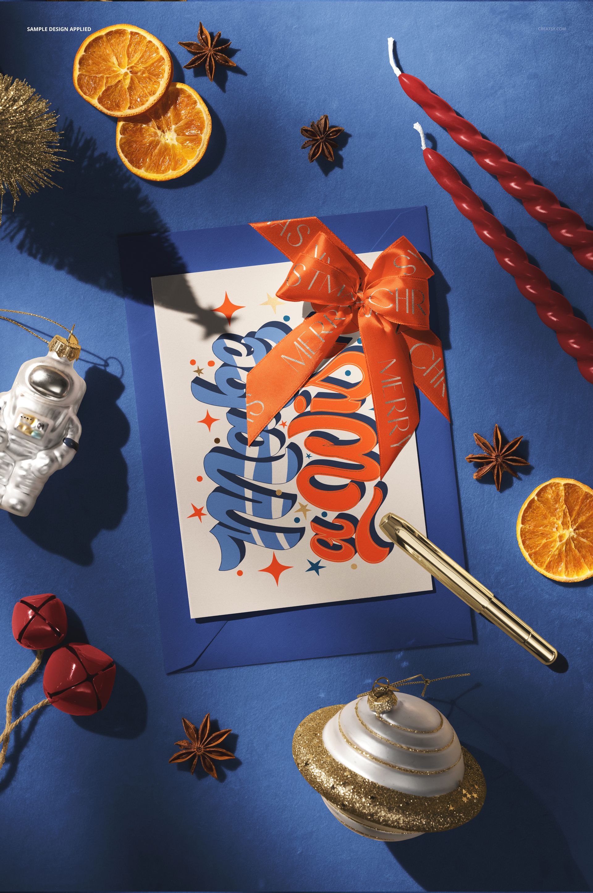 Top view of a Christmas card mockup on a blue surface, featuring dried orange slices, candles, and holiday ornaments.