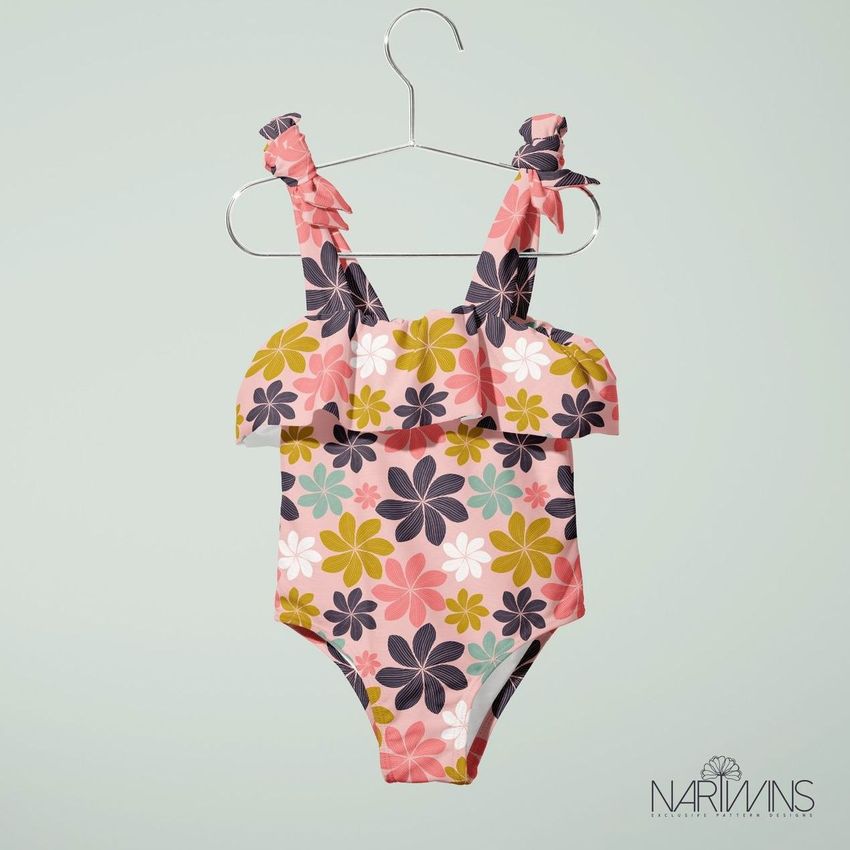 Baby swimsuit mockup featuring a floral pattern in pink, yellow, and dark gray, hanging on a metal hanger against a pale background.