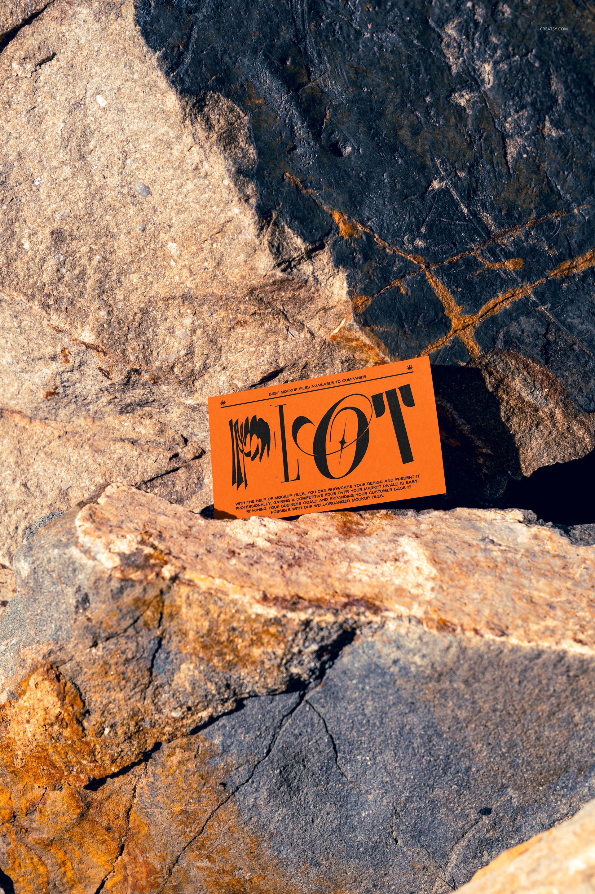Orange business card mockup displayed on textured rusty rocks, shown from a front angle in natural light.