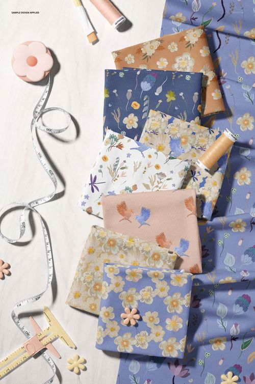 PSD mockup showing various patterned jersey fabrics and sewing tools, including thread spools and measuring tape.