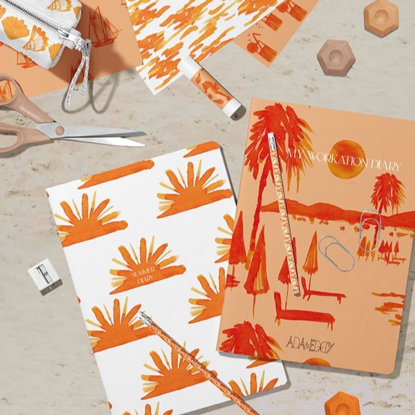 Stationery mockup featuring two classic A4 notebooks with orange and white covers, pencils, and various office supplies on a marble surface.