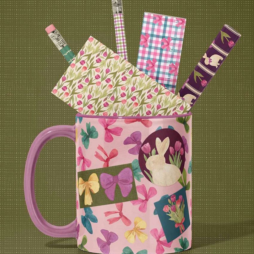 Mug mockup featuring a pink handle and decorated with bows, tulips, and bunny illustrations, filled with patterned stationery items.