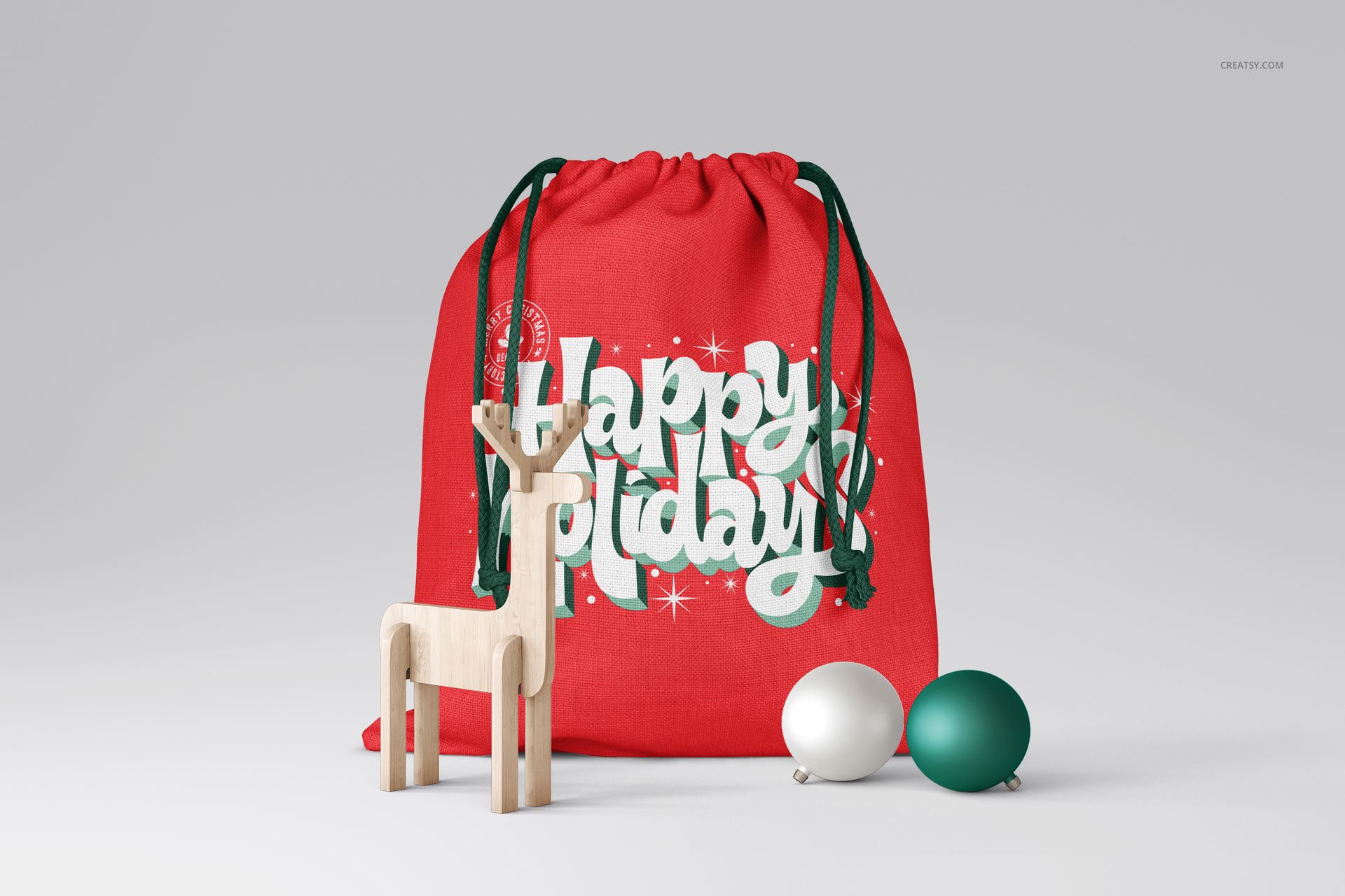 PSD mockup of a Christmas sack in red with green strings, holiday text, and decorative props including a reindeer and ornaments.