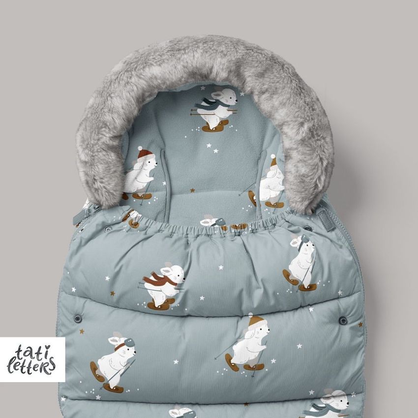 Footmuff mockup featuring a light blue padded cover with playful bunny illustrations in winter outfits, shown on a plain background.