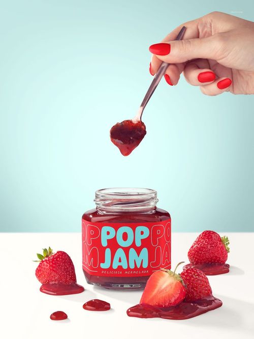 Strawberry jam jar mockup with bold red label, fresh strawberries, and a hand lifting jam with a spoon.