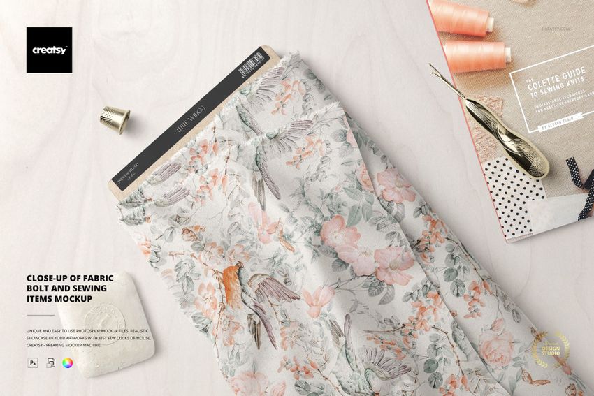 PSD mockup of a patterned fabric bolt placed on a table with sewing accessories and a craft book in the background.