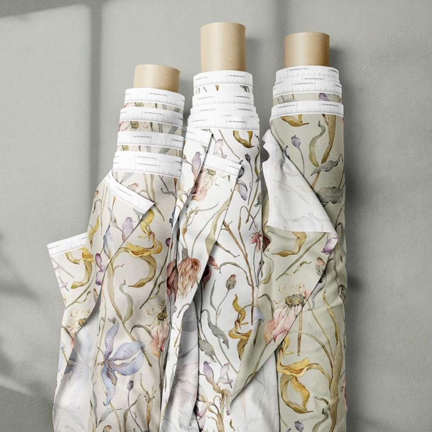Fabric rolls mockup showing three upright rolls wrapped in floral seamless patterns with soft beige and pastel colors against a gray wall.