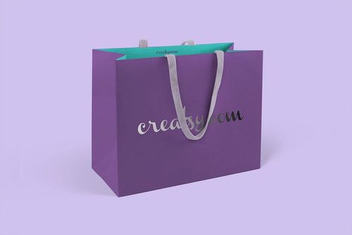 Purple paper bag mockup with silver lettering and gray handles, displayed on a pastel lavender surface.
