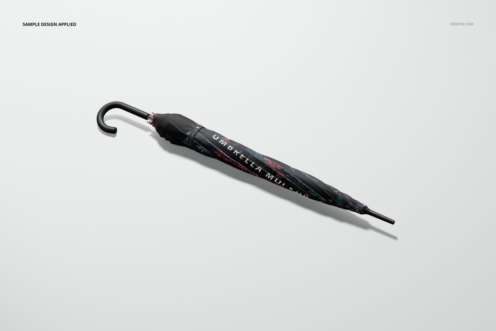 Folded umbrella mockup with black handle and dark patterned cover, shown from a side view on a plain surface.