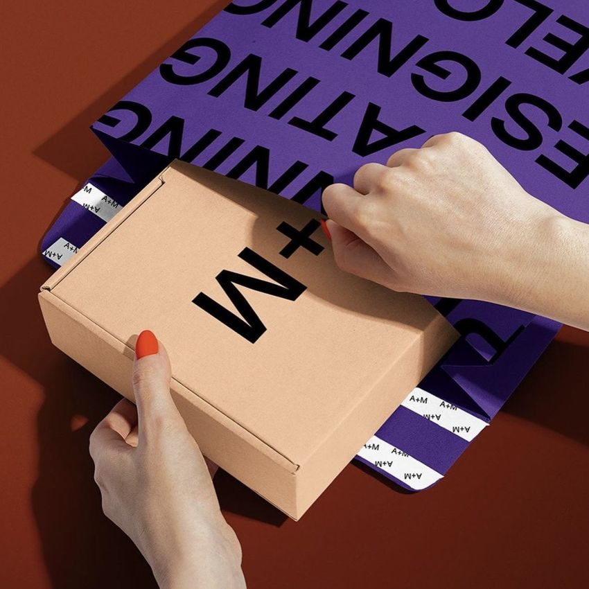Kraft mailer mockup featuring a cardboard box and a purple envelope with black text, shown on a brown background.
