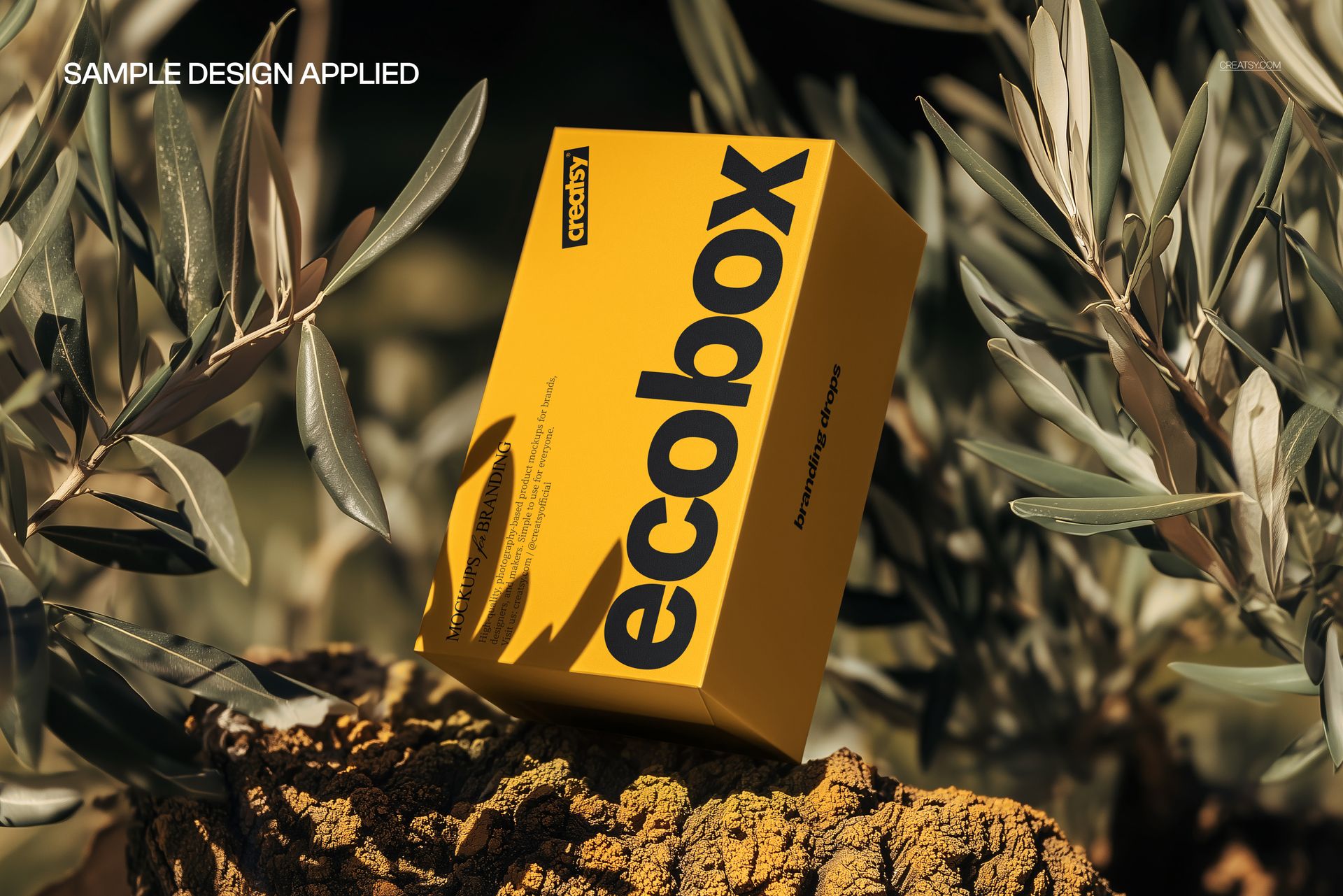 Yellow packaging box mockup with bold black lettering, placed on textured rock with leafy branches in the background.
