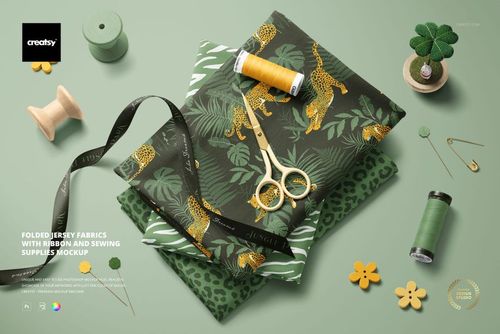 Jersey fabric mockup showing stacked animal print textiles, ribbon, gold scissors, spools, and decorative sewing items.