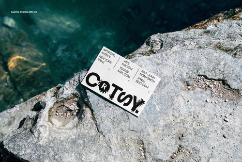 Rectangular business card mockup resting on a sunlit sea cliff, with textured stone and clear blue water nearby.