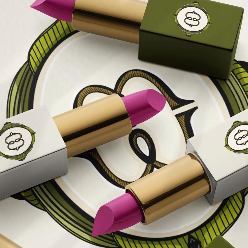 Lipstick mockup featuring three open tubes with gold, olive green, and white casings, arranged on a decorative background.