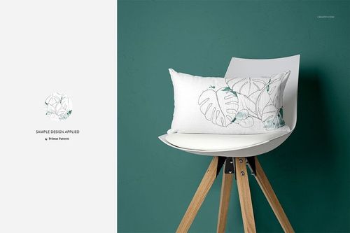 PSD mockup featuring a white pillow with botanical leaf design on a wooden-legged white chair beside a green wall.