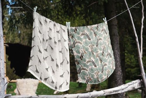 PSD mockup showing two muslin cloths with giraffe and leafy designs hanging in a natural forest environment.