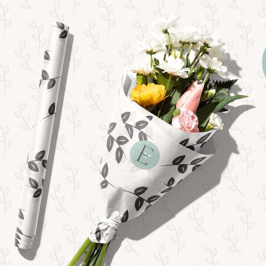 Packaging mockup showing a bouquet of fresh flowers wrapped in white paper with a black leaf pattern and a circular label.