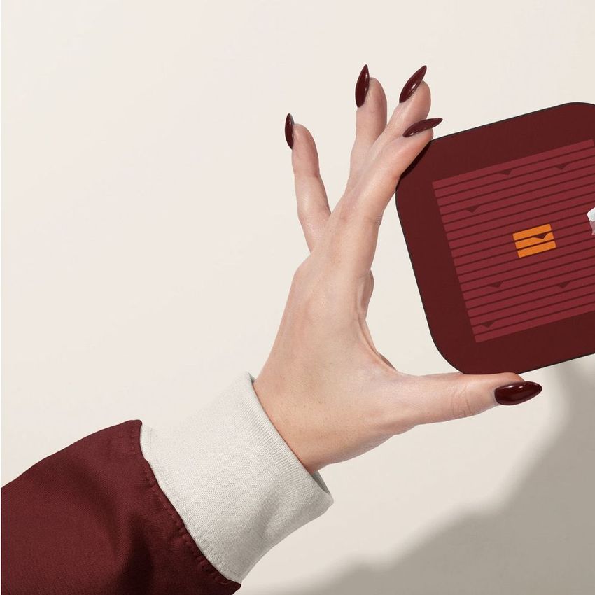 Hand holding a square restaurant branding mockup with maroon and orange design elements against a light background.