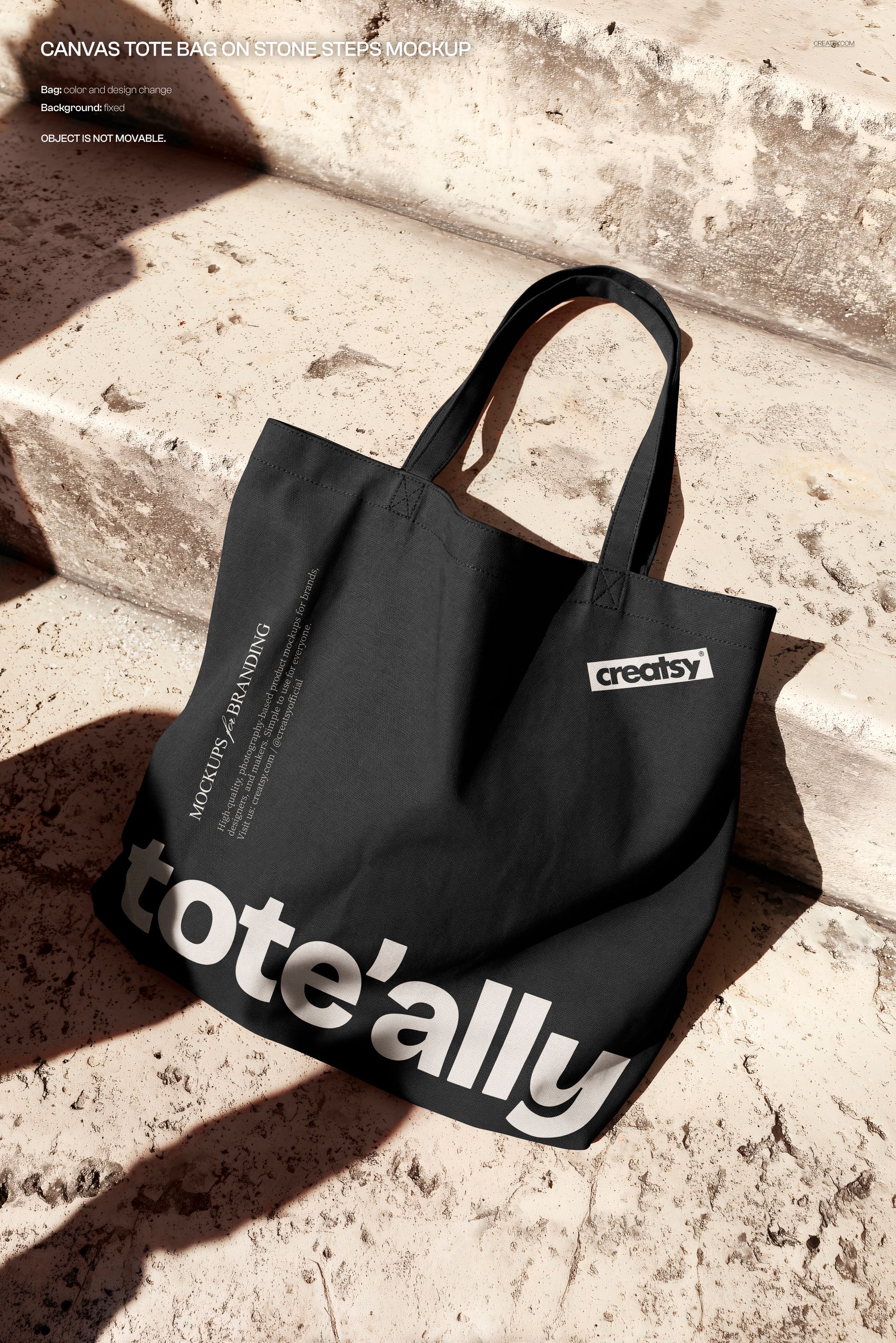 Front-facing black tote bag mockup featuring large white lettering, resting on textured stone stairs in sunlight.