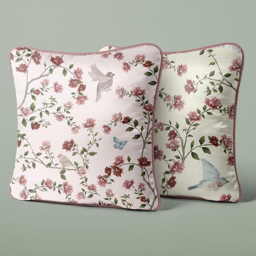 Silk cushion mockup featuring two square pillows with pink braid edges, floral patterns, and bird illustrations on a muted green background.