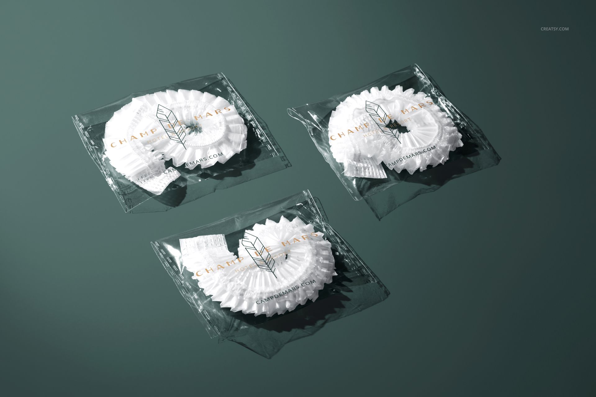 PSD mockup featuring three individually wrapped hotel shower caps arranged on a flat, dark green surface.