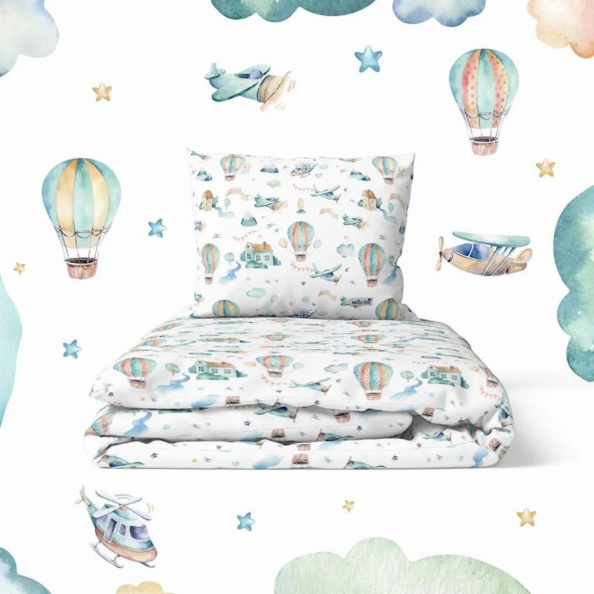 Bedding set mockup featuring a pillow and comforter with watercolor hot air balloons, planes, and clouds on a white background.