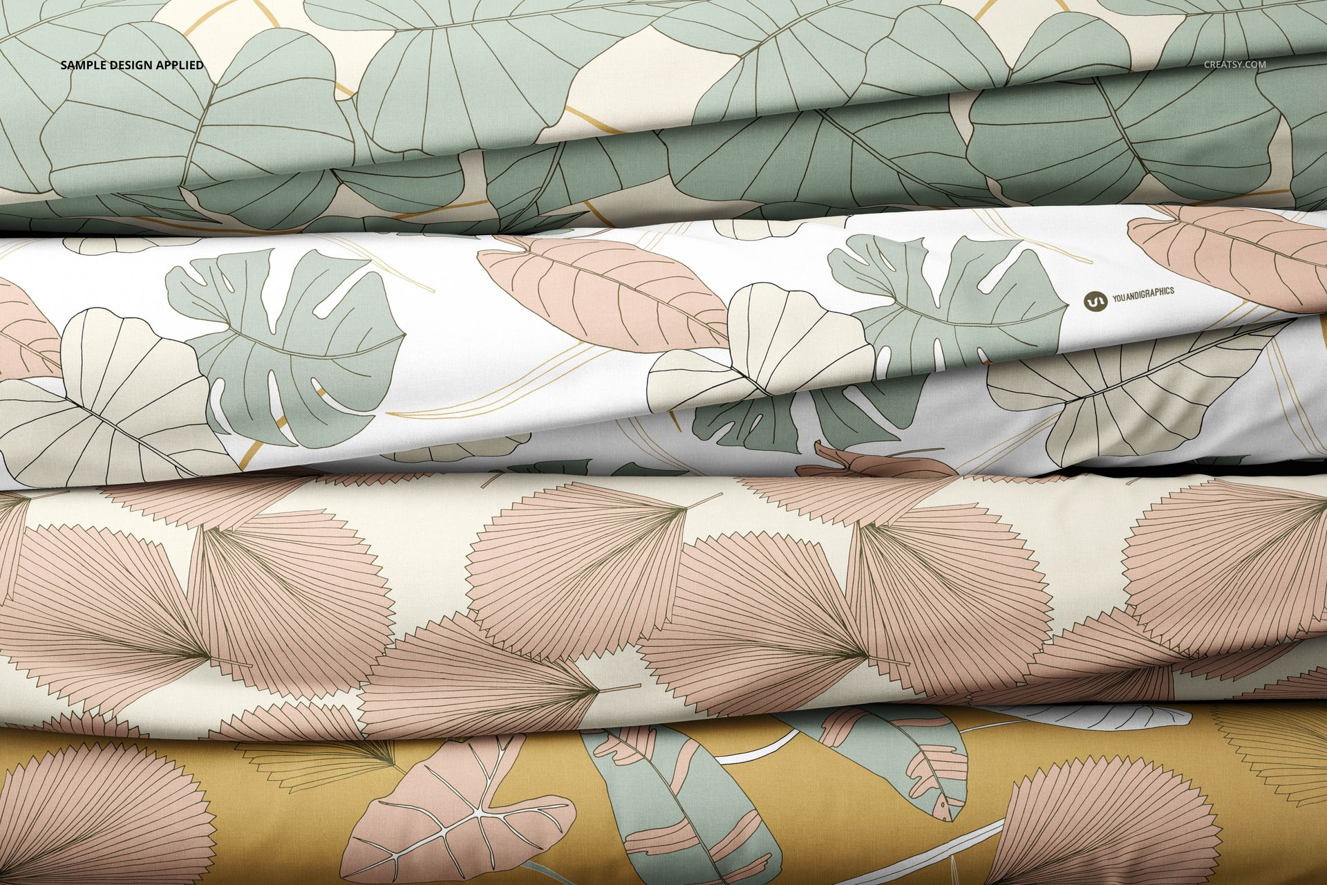 Fabric stack mockup with overlapping textiles displaying tropical and palm leaf motifs in earthy colors.