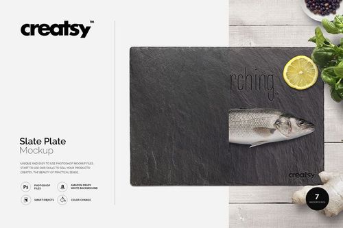 Top view of a dark slate plate mockup featuring a whole fish, lemon wedge, and leafy greens on a wooden background.