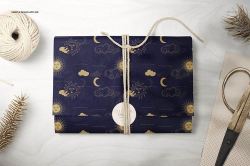 Celestial-themed gift wrapping tissue paper mockup, presented flat and tied with string, with pine branches and craft tools nearby.