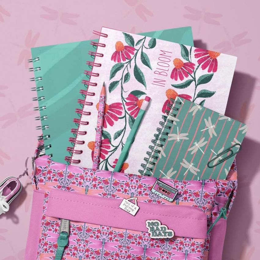School backpack mockup with spiral notebooks, a pencil, and a pen arranged inside an open pink patterned bag on a pink background.