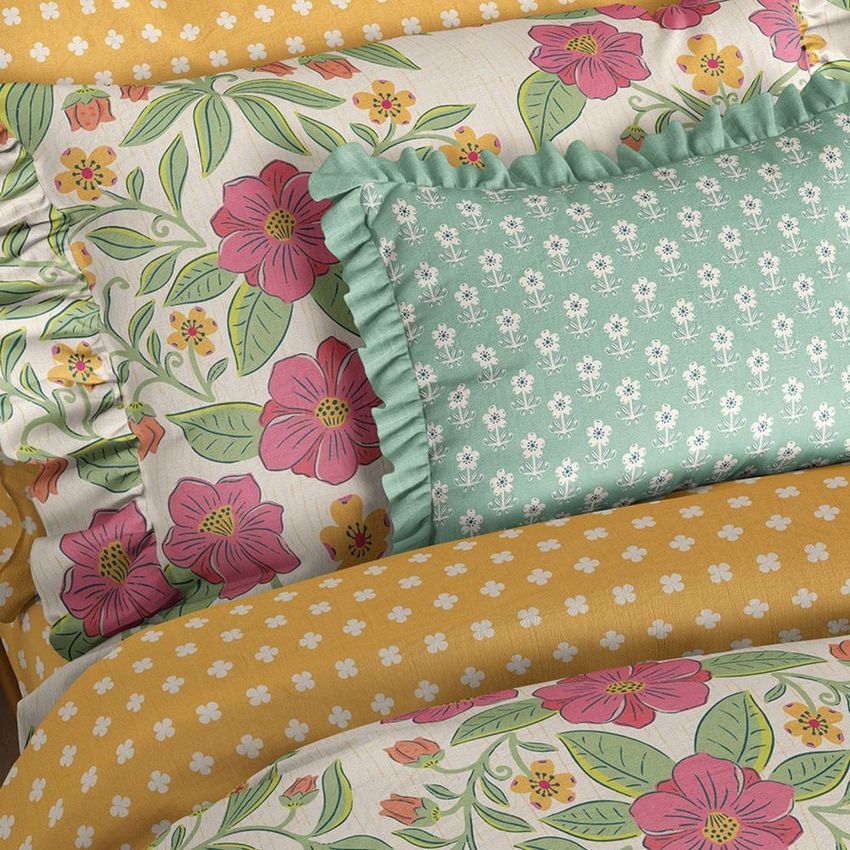 Ruffled pillows and duvet covers mockup featuring floral and patterned designs in pink, green, and yellow tones on a bed.