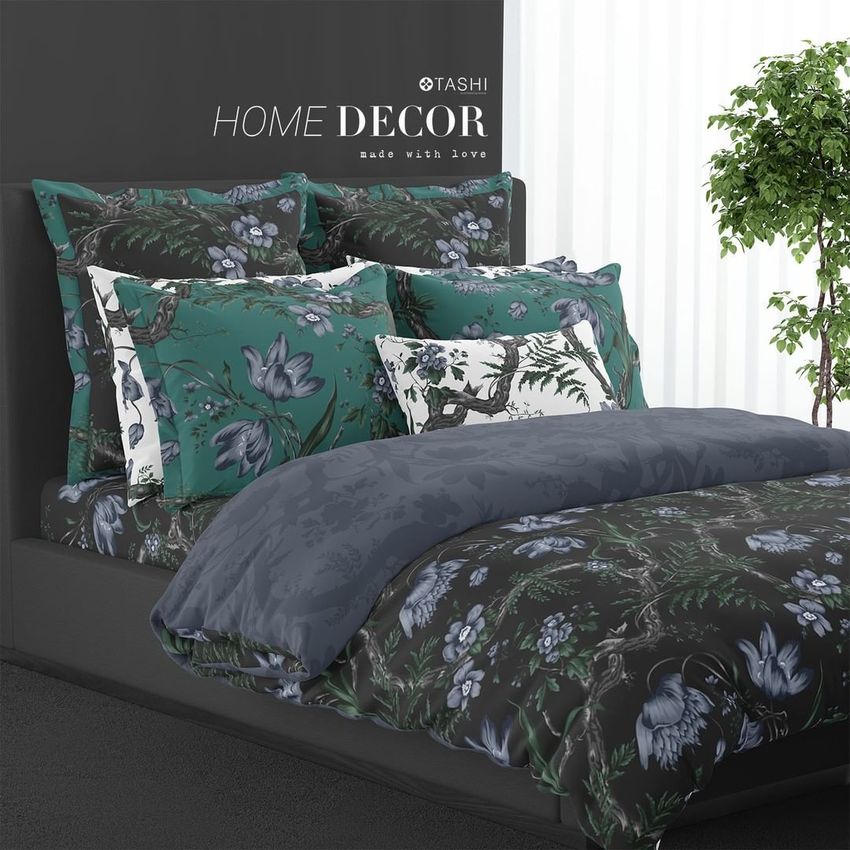 Bedding mockup featuring a neatly made bed with floral patterned duvet and pillows in green, blue, and black tones, set against a dark wall with a potted plant nearby.