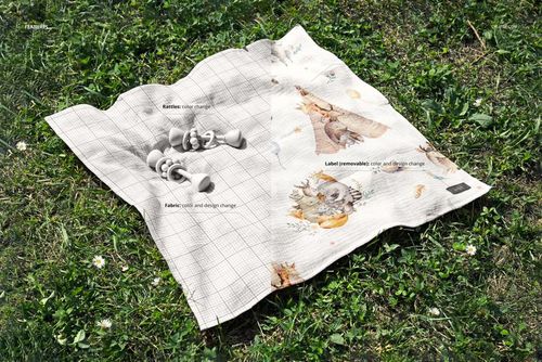 Top view of a crinkled muslin swaddle blanket mockup on grass, featuring customizable label and two rattles.