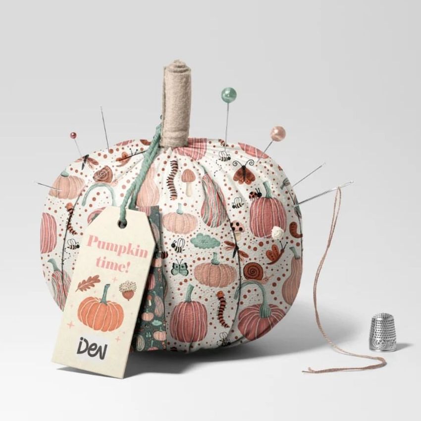 Fabric pumpkin mockup with a pastel pumpkin and leaf pattern, used as a pincushion with sewing pins and a tag attached.