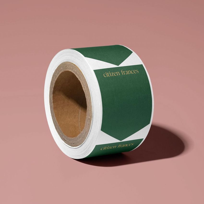 Packing tape mockup featuring a roll of tape with a green and white geometric design and gold text on a pink background.