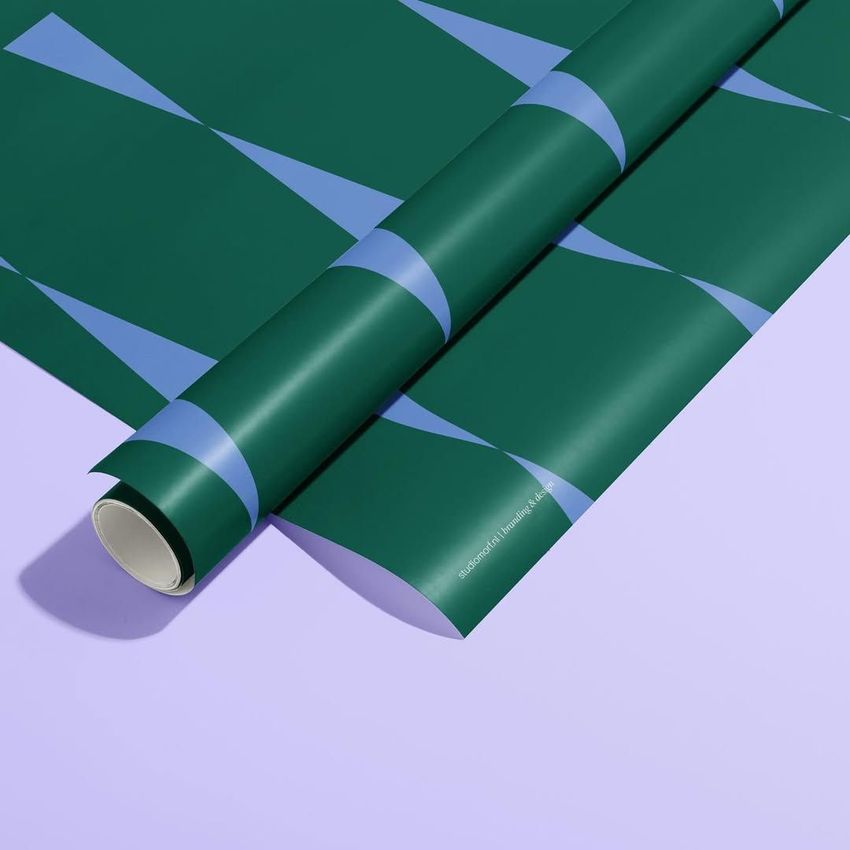 Gift wrapping paper mockup featuring a rolled sheet with a geometric pattern in green and blue on a light purple surface.