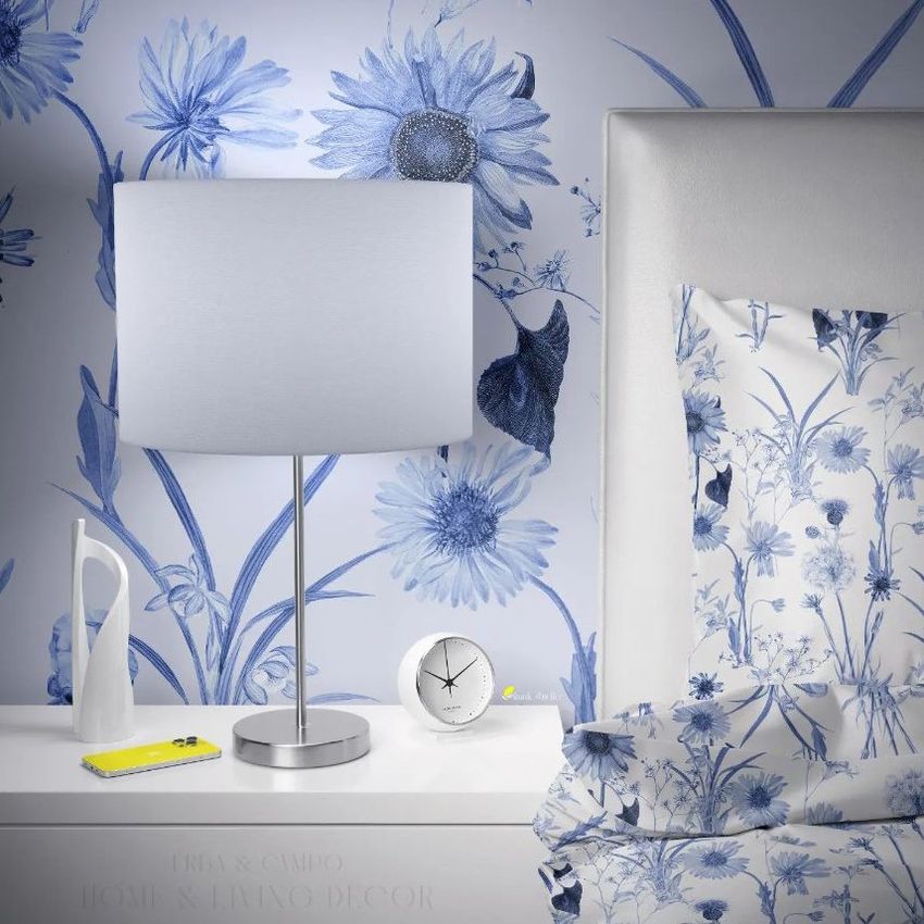 Bedroom wallpaper mockup showing a bedside table with a silver lamp, floral wallpaper, and matching floral bedding in blue and white.