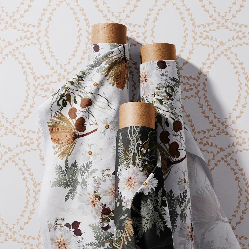 Fabric rolls mockup showing three upright rolls with botanical patterns in muted tones, set against a decorative wallpaper background.