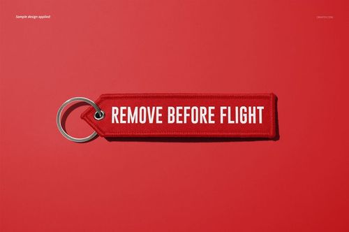 Mockup of a remove before flight keychain in red with white text, shown flat with a metal ring on a plain red surface.