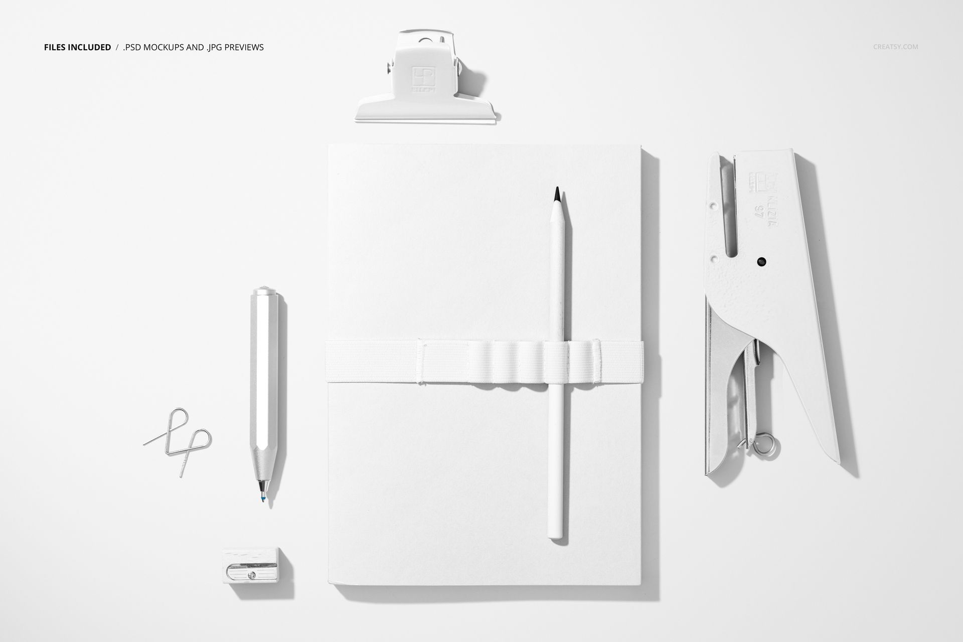 Top view of a stationery mockup featuring a white notebook, pencil, paper clip, pen, and stapler on a light background.