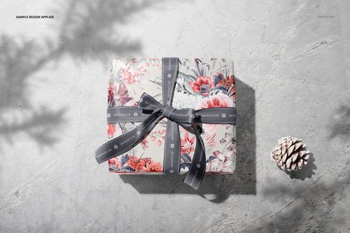 Top view of a mockup gift box with colorful floral wrapping paper and a gray ribbon, placed on a textured background.