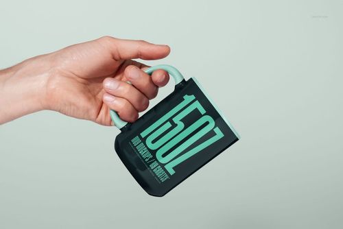 PSD mockup featuring a 15oz mug in black with mint green accents and oversized text, displayed in a hand.